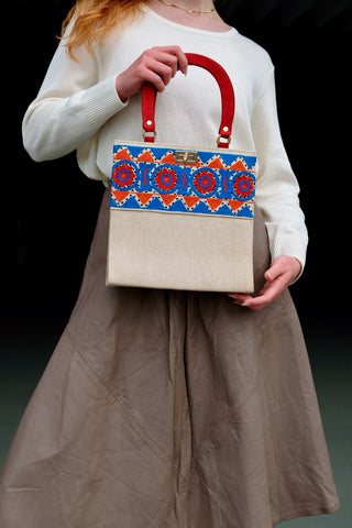 Cremeweiße/Beige Preloved (Secondhand) Handmade Handtasche im Vintage Stil von der Fair Trade Marke Aarong aus Bangladesch, die ländliche Kunsthandwerker unterstützt. Die Marke ist eine soziale Initiative der gemeinnützigen Organisation BRAC International. Die Tasche hat eine hübsche quadratische Form mit roten Henkeln und ist mit tollen Stickereien in Blau, Orange und Rot sowie kleinen schwarzen Pailletten verziert. Mit einem kleinen Innenfach, das mit einem Reißverschluss ausgestattet ist.