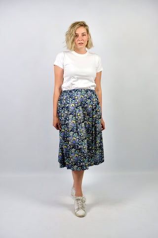 dunkelblauer 80s High Waist Rock aus Materialmix mit Baumwolle- und Modal-Anteil, stretchy Gummizug in der Taille, seitliche Eingrifftaschen und süßes Blümchenmuster in Grau, Mauve, Flieder, Gelb, Türkis, und (Creme)weiß – tragbar von einer XL bis XXL