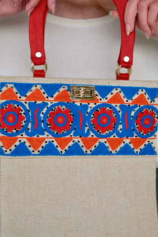 Cremeweiße/Beige Preloved (Secondhand) Handmade Handtasche im Vintage Stil von der Fair Trade Marke Aarong aus Bangladesch, die ländliche Kunsthandwerker unterstützt. Die Marke ist eine soziale Initiative der gemeinnützigen Organisation&nbsp;BRAC International. Die Tasche hat eine hübsche quadratische Form mit roten Henkeln und ist mit tollen Stickereien in Blau, Orange und Rot sowie kleinen schwarzen Pailletten verziert. Mit einem kleinen Innenfach, das mit einem Reißverschluss ausgestattet ist.