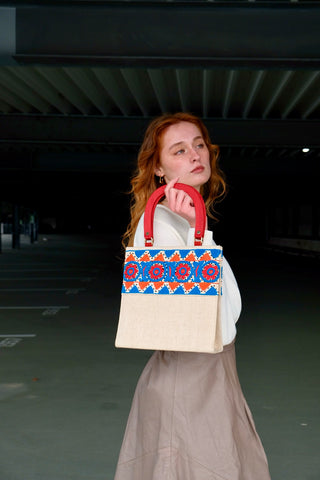 Cremeweiße/Beige Preloved (Secondhand) Handmade Handtasche im Vintage Stil von der Fair Trade Marke Aarong aus Bangladesch, die ländliche Kunsthandwerker unterstützt. Die Marke ist eine soziale Initiative der gemeinnützigen Organisation&nbsp;BRAC International. Die Tasche hat eine hübsche quadratische Form mit roten Henkeln und ist mit tollen Stickereien in Blau, Orange und Rot sowie kleinen schwarzen Pailletten verziert. Mit einem kleinen Innenfach, das mit einem Reißverschluss ausgestattet ist.