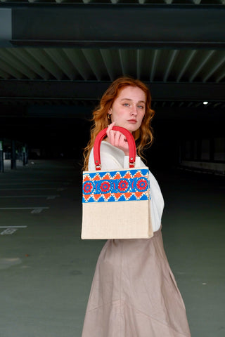 Cremeweiße/Beige Preloved (Secondhand) Handmade Handtasche im Vintage Stil von der Fair Trade Marke Aarong aus Bangladesch, die ländliche Kunsthandwerker unterstützt. Die Marke ist eine soziale Initiative der gemeinnützigen Organisation&nbsp;BRAC International. Die Tasche hat eine hübsche quadratische Form mit roten Henkeln und ist mit tollen Stickereien in Blau, Orange und Rot sowie kleinen schwarzen Pailletten verziert. Mit einem kleinen Innenfach, das mit einem Reißverschluss ausgestattet ist.