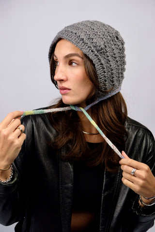 Handmade Bonnet aus Acryl-Garn in Grau mit bunten, schmalen Bindebändern.