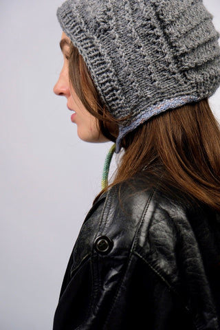 Handmade Bonnet aus Acryl-Garn in Grau mit bunten, schmalen Bindebändern.