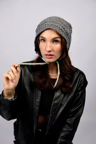 Handmade Bonnet aus Acryl-Garn in Grau mit bunten, schmalen Bindebändern.