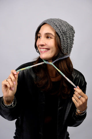Handmade Bonnet aus Acryl-Garn in Grau mit bunten, schmalen Bindebändern.