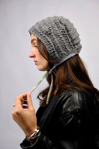 Handmade Bonnet aus Acryl-Garn in Grau mit bunten, schmalen Bindebändern.