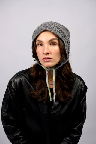 Handmade Bonnet aus Acryl-Garn in Grau mit bunten, schmalen Bindebändern.