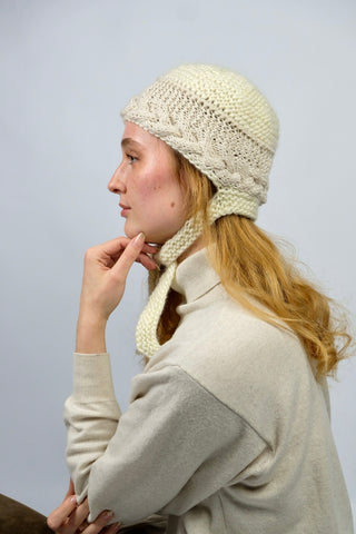 Handmade Bonnet aus Schurwolle-Mix-Garn in Cremeweiß mit Zopfstrickbündchen in Beige und Bindebändern.