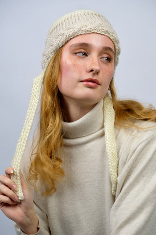 Handmade Bonnet aus Schurwolle-Mix-Garn in Cremeweiß mit Zopfstrickbündchen in Beige und Bindebändern.