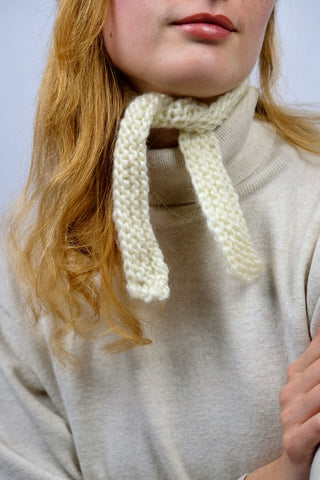 Handmade Bonnet aus Schurwolle-Mix-Garn in Cremeweiß mit Zopfstrickbündchen in Beige und Bindebändern.