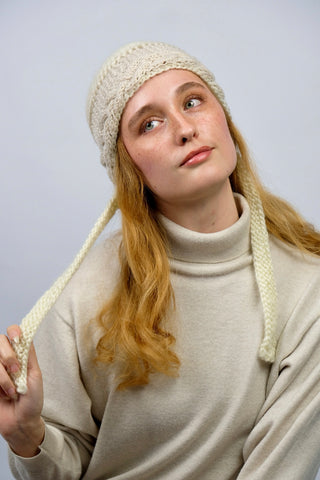 Handmade Bonnet aus Schurwolle-Mix-Garn in Cremeweiß mit Zopfstrickbündchen in Beige und Bindebändern.
