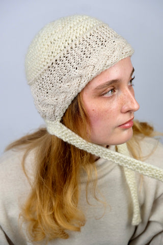 Handmade Bonnet aus Schurwolle-Mix-Garn in Cremeweiß mit Zopfstrickbündchen in Beige und Bindebändern.