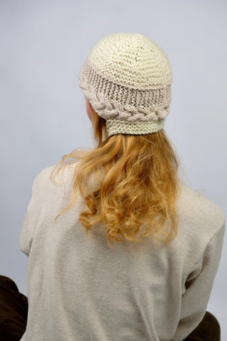 Handmade Bonnet aus Schurwolle-Mix-Garn in Cremeweiß mit Zopfstrickbündchen in Beige und Bindebändern.