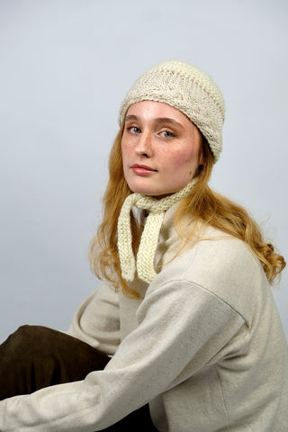 Handmade Bonnet aus Schurwolle-Mix-Garn in Cremeweiß mit Zopfstrickbündchen in Beige und Bindebändern.