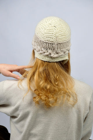 Handmade Bonnet aus Schurwolle-Mix-Garn in Cremeweiß mit Zopfstrickbündchen in Beige und Bindebändern.