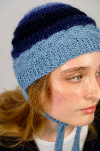 Handmade Bonnet aus Schurwolle- und Mohair-Mix Garn in Blautönen mit Zopfstrickmuster und Bindebändern.