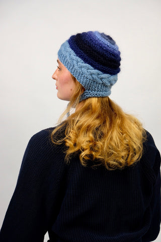 Handmade Bonnet aus Schurwolle- und Mohair-Mix Garn in Blautönen mit Zopfstrickmuster und Bindebändern.