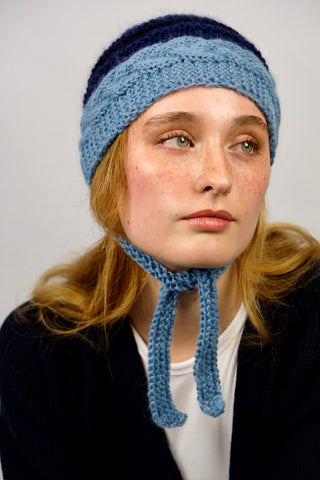 Handmade Bonnet aus Schurwolle- und Mohair-Mix Garn in Blautönen mit Zopfstrickmuster und Bindebändern.