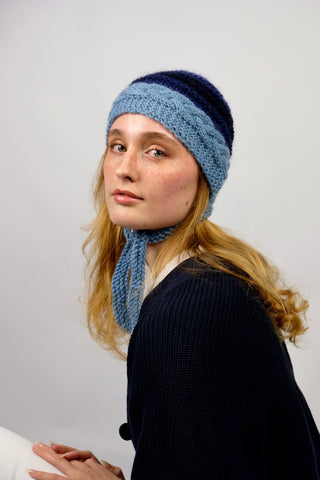 Handmade Bonnet aus Schurwolle- und Mohair-Mix Garn in Blautönen mit Zopfstrickmuster und Bindebändern.