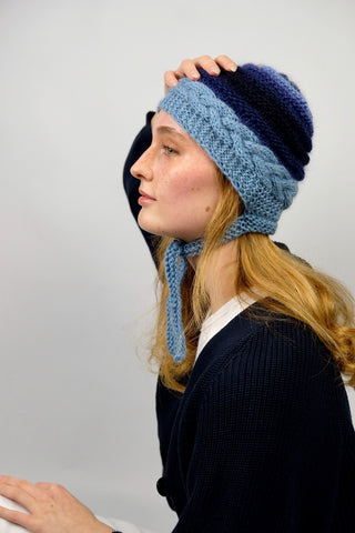 Handmade Bonnet aus Schurwolle- und Mohair-Mix Garn in Blautönen mit Zopfstrickmuster und Bindebändern.