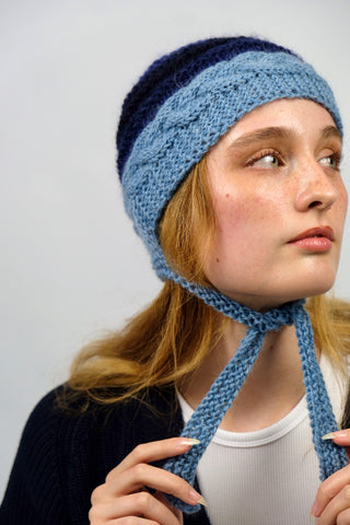 Handmade Bonnet aus Schurwolle- und Mohair-Mix Garn in Blautönen mit Zopfstrickmuster und Bindebändern.