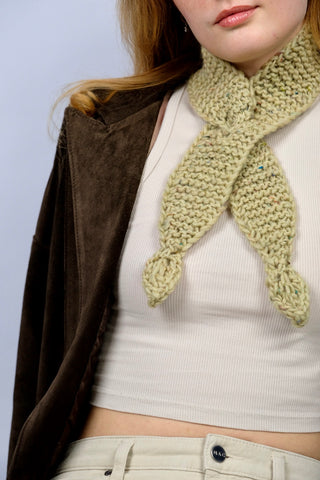 Handmade Minischal im Ascot-Stil aus pistaziengrünem, leicht meliertem Tweed-Garn mit Blatt-Details an den Enden. Wird durch eine kleine Öffnung auf einer Seite gesteckt, um ihn sicher am Hals zu halten.