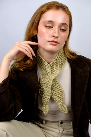 Handmade Minischal im Ascot-Stil aus pistaziengrünem, leicht meliertem Tweed-Garn mit Blatt-Details an den Enden. Wird durch eine kleine Öffnung auf einer Seite gesteckt, um ihn sicher am Hals zu halten.