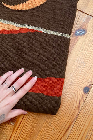 Dunkelbrauner 90s Pullover mit Stehkragen und tollem Grafikmuster in Orange, Rot, Beige und Gold – die angegebene Größe ist L, für einen lockeren Look empfehlen wir den Pullover jedoch eher einer heutigen M oder der Zwischengröße S/M