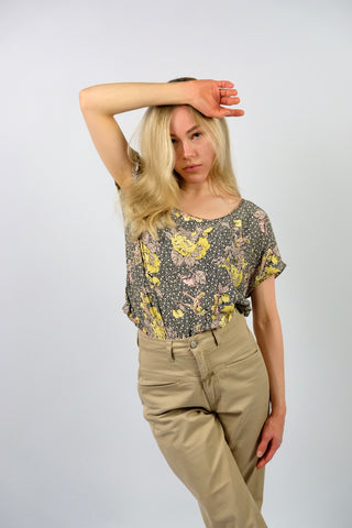 Locker, kurz und boxy geschnittenes 80s Viskose Shirt mit weitem Rundhalskragen, Knopfleiste am Rücken und tollem Blumenmuster in Schwarz, Weiß, Graubraun, Rosa und gedeckten Gelbtönen – wir empfehlen das Shirt einer S bis M