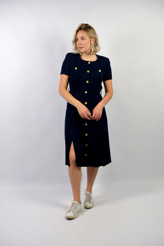 Elegantes, dunkelblaues 80s/90s Kleid made in Italy mit durchgehender Knopfleiste, leichten Schulterpolstern (welche je nach Belieben auch einfach herausgetrennt werden könnten) und Beinschlitzen – die angegebene Größe ist L, fällt unserer Einschätzung nach etwas kleiner aus: wir empfehlen das Kleid einer heutigen M oder der Zwischengröße M/L