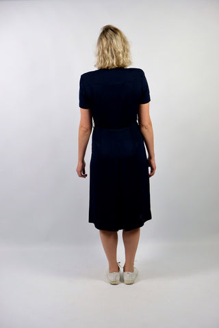 Elegantes, dunkelblaues 80s/90s Kleid made in Italy mit durchgehender Knopfleiste, leichten Schulterpolstern (welche je nach Belieben auch einfach herausgetrennt werden könnten) und Beinschlitzen – die angegebene Größe ist L, fällt unserer Einschätzung nach etwas kleiner aus: wir empfehlen das Kleid einer heutigen M oder der Zwischengröße M/L