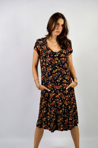 dunkelblaues 80s/90s Viskose Kleid in lockerem Schnitt mit aufgesetzten Taschen, leichten Schulterpolstern (welche je nach Belieben auch einfach herausgetrennt werden könnten) sowie Blümchenmuster in Gelb, Rot, Orange, Weiß und Grüntönen – wir empfehlen das Kleid einer S/M oder kleinen M je nach gewünschter Passform