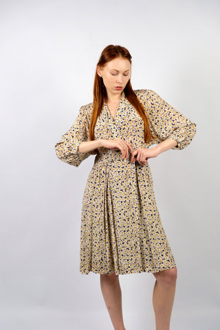 80s Blusenkleid mit V-Kragen, Wickeloptik, seitlichen Eingrifftaschen und Blümchenmuster in Schwarz/Braunschwarz, Creme, Greige (Mix aus Grau und Beige), Gelb und Orange – im oberen Bereich entspricht das Kleid einer heutigen S, die Taille fällt eher locker aus, weshalb wir es einer S oder der Zwischengröße S/M empfehlen (bitte Maße beachten) – ein absolutes Highlight