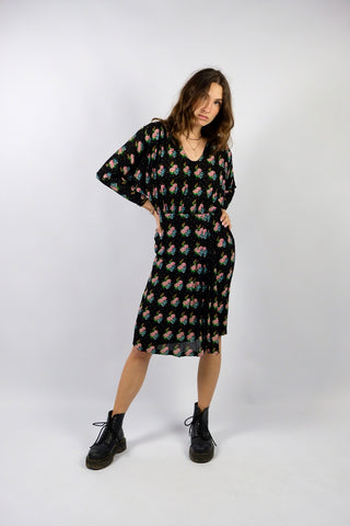 Schwarzes Handmade 70s/80s Kleid in tailliertem Schnitt mit weitem Design oben und zweilagiger Optik unten sowie süßem floralem Muster in Türkis, Grün, Pink/Rosa, Orange und Weiß – fällt im unteren Bereich eher schmal aus, weshalb wir es einer XS empfehlen (bei Bedarf kann es auch toll mit einem Gürtel kombiniert werden) – ein wahres Unikat und absolutes Highlight