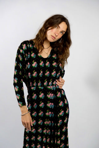 Schwarzes Handmade 70s/80s Kleid in tailliertem Schnitt mit weitem Design oben und zweilagiger Optik unten sowie süßem floralem Muster in Türkis, Grün, Pink/Rosa, Orange und Weiß – fällt im unteren Bereich eher schmal aus, weshalb wir es einer XS empfehlen (bei Bedarf kann es auch toll mit einem Gürtel kombiniert werden) – ein wahres Unikat und absolutes Highlight