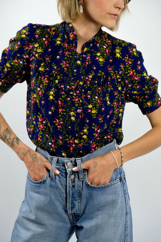 Dunkelblaue Handmade 70s Bluse mit kleinem Stehkragen, leichten Puffärmeln und Blümchenmuster in Grün, Gelb, Rot, Pink und Weiß – wir empfehlen die Bluse einer XXS