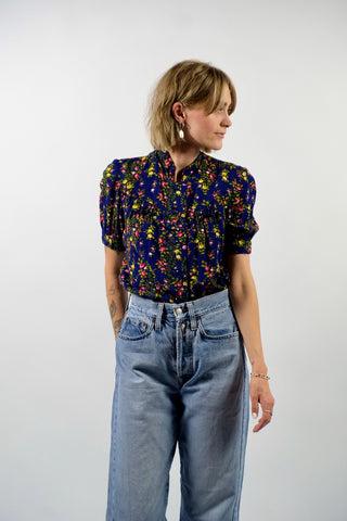 Dunkelblaue Handmade 70s Bluse mit kleinem Stehkragen, leichten Puffärmeln und Blümchenmuster in Grün, Gelb, Rot, Pink und Weiß – wir empfehlen die Bluse einer XXS