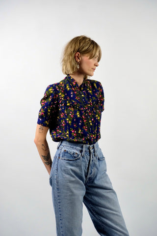 Dunkelblaue Handmade 70s Bluse mit kleinem Stehkragen, leichten Puffärmeln und Blümchenmuster in Grün, Gelb, Rot, Pink und Weiß – wir empfehlen die Bluse einer XXS
