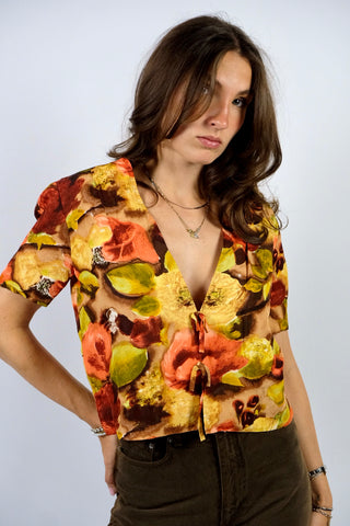Handmade 80s/90s Bluse in kurzem Schnitt mit tiefem V-Kragen, Hakenverschlüssen mit Zierschleifen sowie floralem Crazy Pattern Print in Rotbraun, Braun, Beige, Weinrot, Orange/Pfirsich, Gelb, Gelbgrün und Hellgrün – wir empfehlen die Bluse einer S – ein Unikat und Highlight