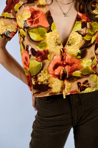 Handmade 80s/90s Bluse in kurzem Schnitt mit tiefem V-Kragen, Hakenverschlüssen mit Zierschleifen sowie floralem Crazy Pattern Print in Rotbraun, Braun, Beige, Weinrot, Orange/Pfirsich, Gelb, Gelbgrün und Hellgrün – wir empfehlen die Bluse einer S – ein Unikat und Highlight